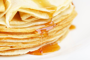 A stack of thin pancakes with honey