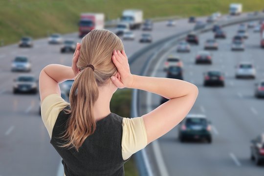 Frau mit Haenden an Ohren vor Autobahn
