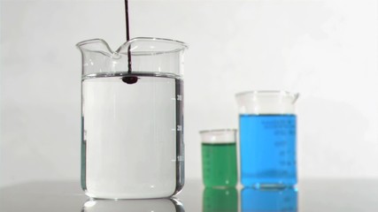 Red droplets in a super slow motion dripping in the water of a beaker - Powered by Adobe