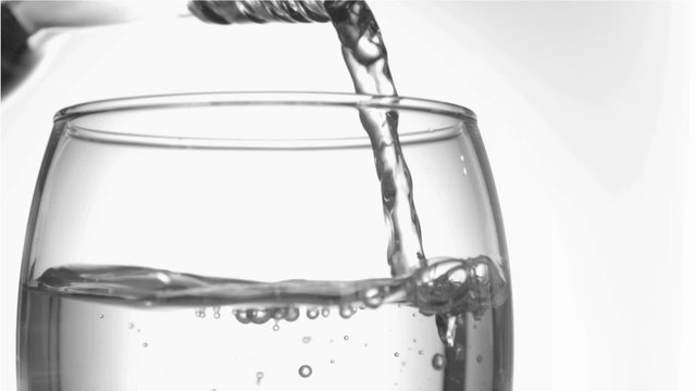 Trickle of water in a super slow motion finishing to serve of the glass bottleneck in a tumbler glas