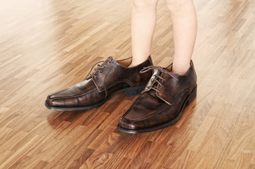 Toddler wearing adult shoes on walnut parquet floor.
