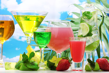 Glasses of cocktails on table on blue sky background