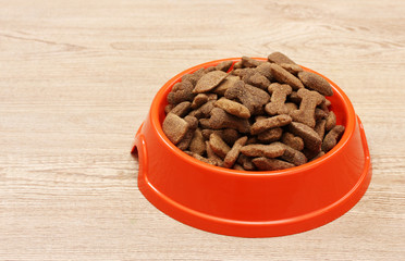dry dog food in orange bowl on wooden background