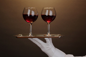 Hand in glove holding silver tray with wineglasses