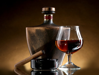 bottle and glass of brandy and cigar on brown background