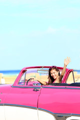 Woman driving convertible car waving happy