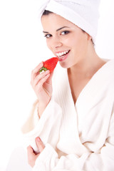 Beautiful woman in a white spa bath robe eating a strawberry