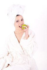 Beautiful young woman in a white spa bath robe eating a apple