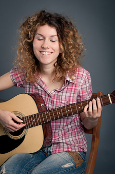 Happy country girl with a guitar against dark background.