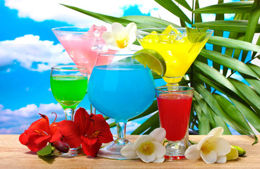 exotic cocktails and flowers on table on blue sky background