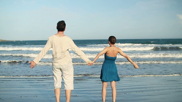 Young couple standing hand in hand on the beach , slow motion