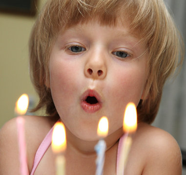 Happy Little Blond Girl Blowing Cake Candle In A Birthday Party