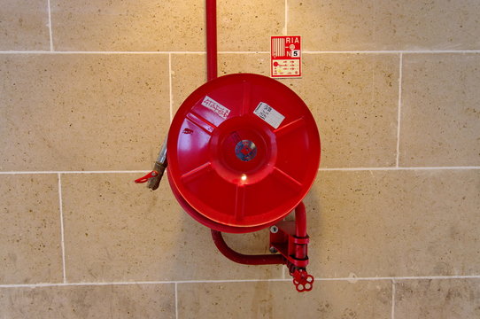 Lance d'incendie rouge enroul&eacute;e sur un mur de pierre.