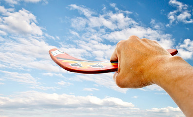 hand holdiing boomerang with blue sky - obrazy, fototapety, plakaty