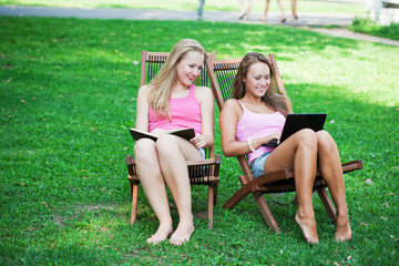 Two girls sit in chaiselounges on  glade with  book and a laptop