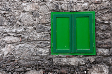stony house wall with a closed green window