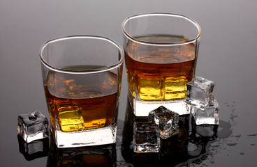 two glasses of scotch whiskey and ice on grey table