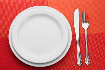 White empty plate with fork and knife on a red tablecloth