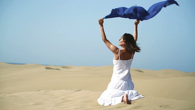 Woman with sarong sitting on the desert, slow motion