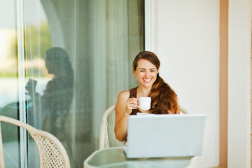 Fototapeta na wymiar Laughing woman enjoying cup of coffee and looking in laptop