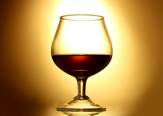 Glass of cognac on yellow background