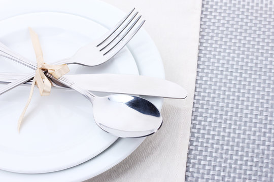 White empty plates with fork, spoon and knife tied with a ribbon