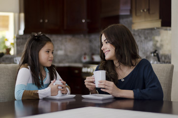 Young mother and daughter having coffee in the kitchen