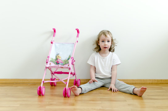 Little cute girl sitting on the floor next to the toy stroller