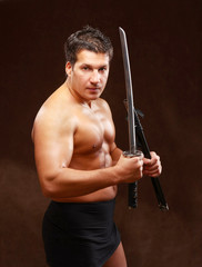 A muscled male posing with a sword on brown background