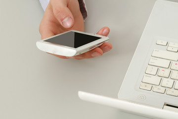 A touchphone in a male hand, near a laptop