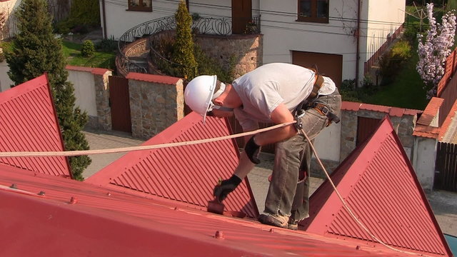 Man paints roof of a private house with safety rope