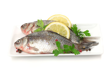 Fresh fishes with lemon and parsley on plate isolated on white