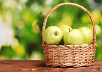 juicy green apples in basket on wooden table on green background