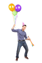 Full length portrait of a happy male holding balloons and a horn