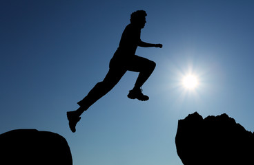 Silhouette of hiking man jumping over the mountains at sunset