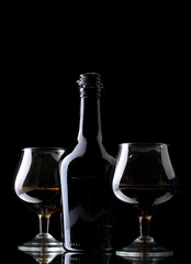 Glasses of brandy and bottle on black background