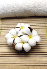 Fototapeta na wymiar Bowl of frangipani flowers and towel on bamboo mat