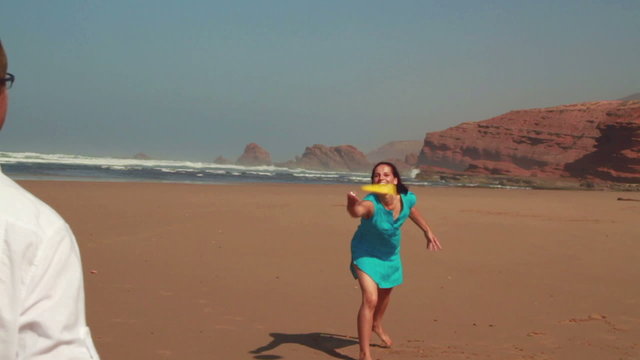 Happy couple having fun with freesby on the beach, slow motion