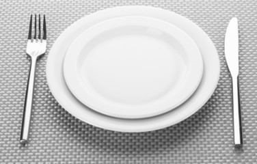 White empty plates with fork and knife on a grey tablecloth