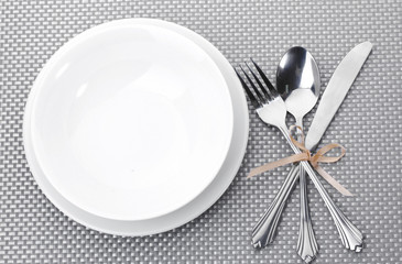 White empty plates with fork, spoon and knife tied with a ribbon