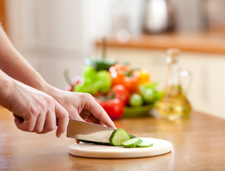 Male hands cutting of cucumer on hardboard and fresh vegetables