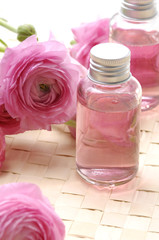 Obraz na płótnie Canvas Pink ranunculus flowers and massage lotion, on woven mat