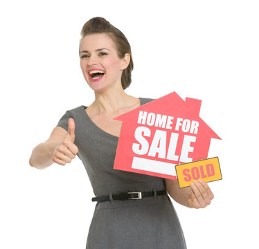 Happy realtor with home for sale sold sign showing thumbs up