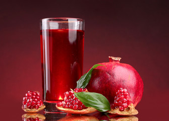 ripe pomergranate and glass of juice on red background