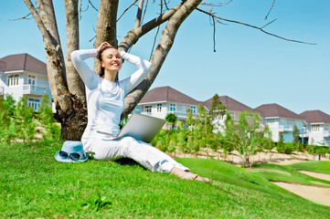 Fototapeta premium Pretty woman sitting by tree with laptop computer