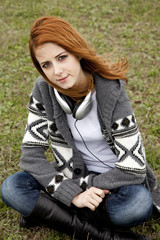 Obraz premium Sad girl with headphones sitting at green spring grass.