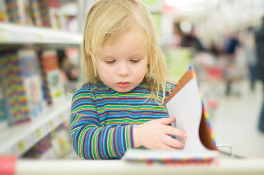 Adorable baby with book near book stand in supermarket
