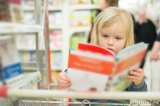 Adorable baby with book near book stand in supermarket