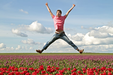 Young enthousiastic guy jumping up from the tulip fields in the