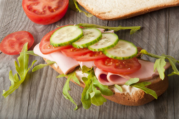 Sandwich with ham, tomato, cucumber and arugula